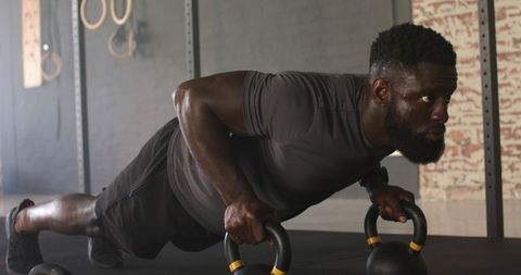 Focused Athlete Planking With Kettlebells in Gym