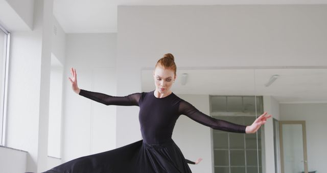 Focused caucasian female ballet dancer in black dress practicing at dance studio. Dance, ballet, discipline, practice and training, unaltered.