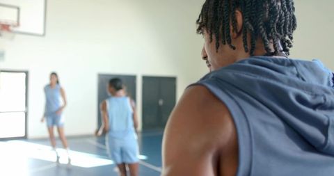 Male player observing teammates during sunlit indoor basketball drill in gymnasium