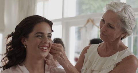 Bride Smiling while Preparing with Supportive Older Woman at Wedding