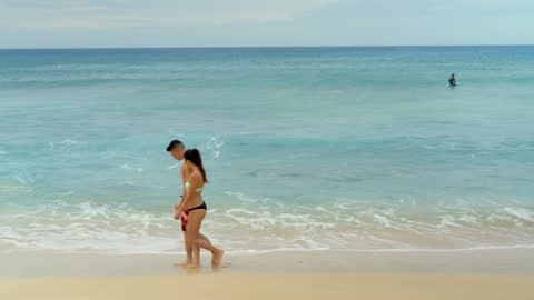Couple Walking on Tropical Beach against Ocean Waves