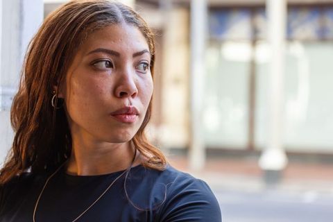 Pensive young woman leaning on column in urban storefront looking right, fashion portrait