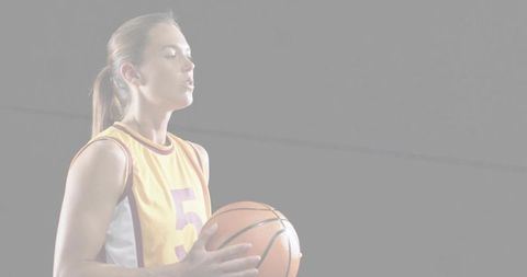 Female basketball player holding ball in yellow jersey number 5 on gray background
