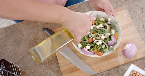 Woman Pouring Olive Oil on Fresh Vegetable Salad in Modern Kitchen