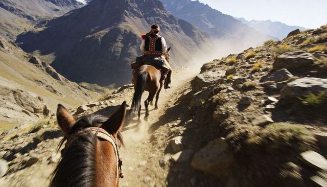 Riding high mountain pass on pack horses with guiding rider in patterned vest