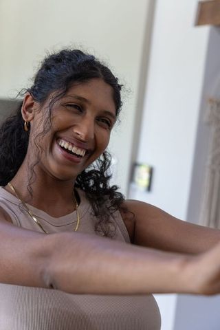 Joyful african american woman reaching out smiling and laughing in casual beige top at home