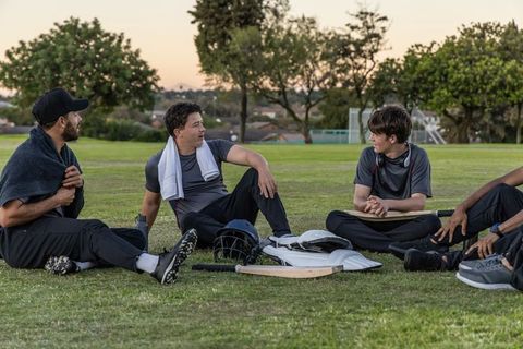 Cricket teammates resting on grass at sunset after match