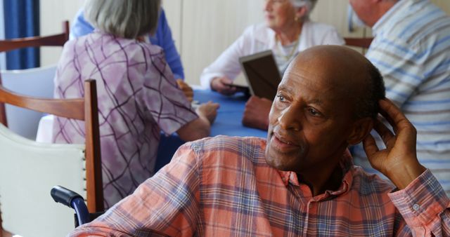 African American elderly man sitting in a communal area of retirement home, engaging with other older adults. Ideal for depicting senior living, aging lifestyle, caregiving services, community life, and social interaction among older adults.