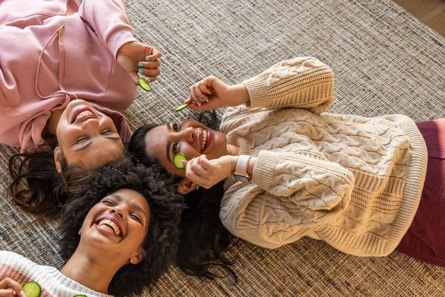 Multicultural friends enjoying cozy at-home spa day laughing and relaxing with cucumber slices