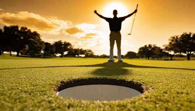 Golfer celebrating on putting green at golden hour raising putter in triumphant silhouette