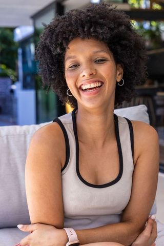 Joyful african american woman laughing on patio wearing ribbed tank and smartwatch