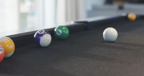 Resting clustered pool balls on dark felt with cue ball in soft daylight lounge scene