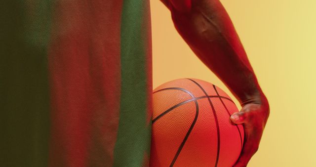 Image of midsection of african american male basketball player holding ball on orange background. Sports and competition concept.