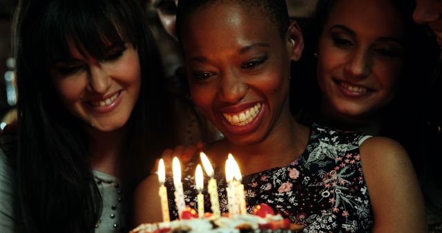 Woman smiling brightly while blowing out candles on birthday cake surrounded by friends. Perfect for illustrating celebrations, friendship, and happy moments.