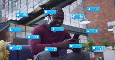 Smiling man checking smartphone while receiving social media notifications in modern loft