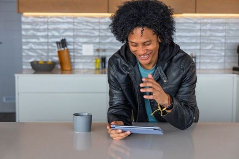 African american man laughing while using tablet on contemporary kitchen countertop with mug