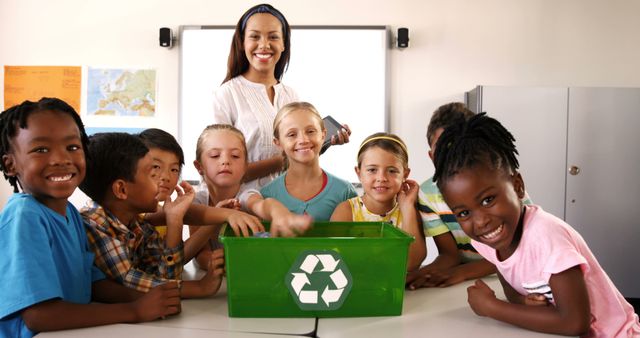 Teacher encouraging group of diverse students to learn about recycling and sustainability in classroom. Smiling children gather around green recycling bin, showing excitement and participation. Suitable for use in educational materials, environmental awareness campaigns, school programs, and diversity promotion images.