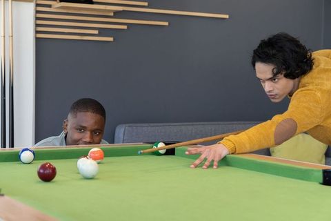 Young diverse men playing pool in modern lounge, focusing on shot and friendly competition