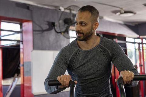 Focused indian man cycling on cardio bike in urban gym, building strength and endurance