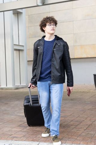 Young traveler walking through urban plaza pulling carry-on suitcase holding passport