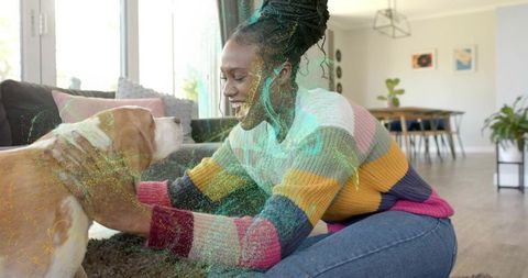 Joyful woman kneeling petting dog in colorful striped sweater in bright living room