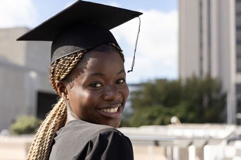 African american graduate smiling while wearing mortarboard and gown on university campus