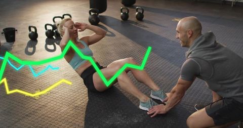 Female athlete performing core workout with personal trainer holding feet and neon graphs