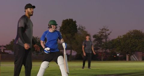 Cricket batsman preparing to face delivery at dusk during team practice on grass field