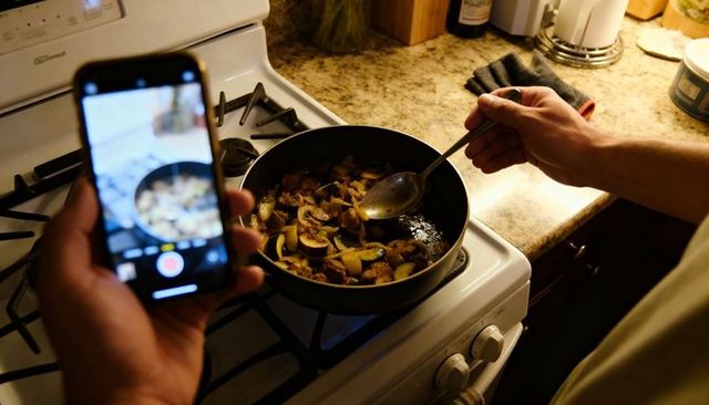 Home cooking recording: stirring mushrooms and vegetables on gas stove with smartphone