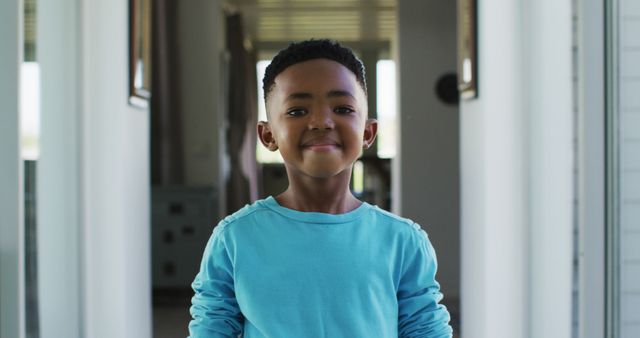Young boy standing indoors, looking into camera with a confident smile. Suitable for use in advertising, educational materials, family-related content, and promotional campaigns showcasing diversity, confidence, and youth.