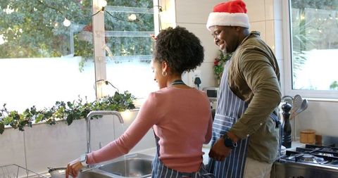 Washing dishes together on sunlit holiday morning wearing striped aprons and santa hat