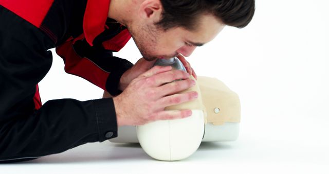 A young Caucasian man is performing CPR on a training manikin, practicing emergency medical procedures, with copy space. His focused expression and the use of a resuscitation aid underscore the importance of life-saving skills.