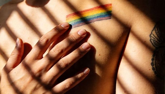 Placing hand over chest with rainbow pride stripes and lace lingerie in sunlit blinds