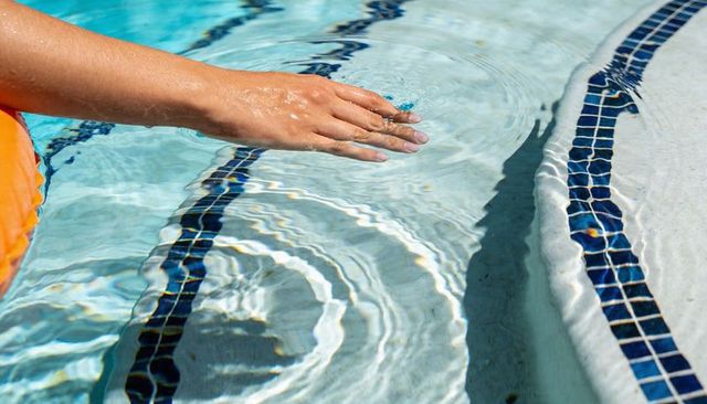 Sunlit hand skimming pool water creating ripples along tiled edge with orange float