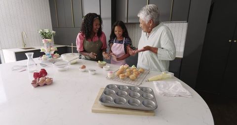 Three generations baking and decorating cupcakes together on marble kitchen island