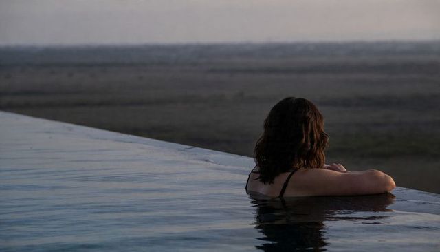 Woman leaning on infinity pool edge gazing at tranquil dusk horizon, solo relaxation