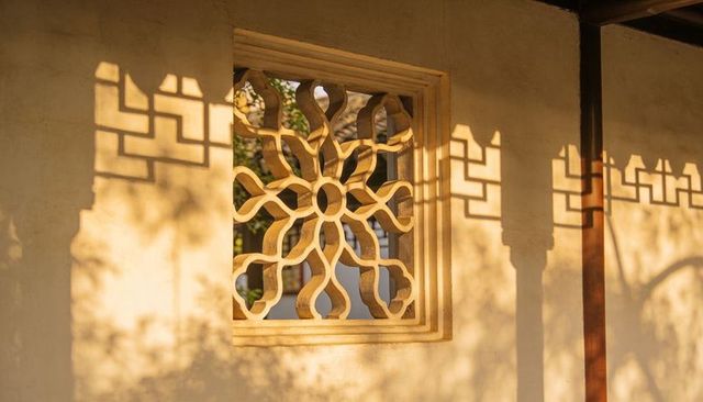 Golden-hour lattice rosette casting intricate decorative shadows on plaster wall, veranda detail