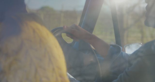 Person sitting in driver's seat, gripping steering wheel under bright sunlight. Captures sense of adventure, travel. Useful for themes related to road trips, driving, journey, outdoors activities, automotive.