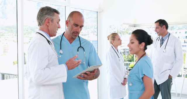 Doctors and medical staff discussing patient care while using a tablet in a bright, modern hospital. Ideal for depicting teamwork, medical consultation, healthcare technology, and collaboration in a clinical setting.