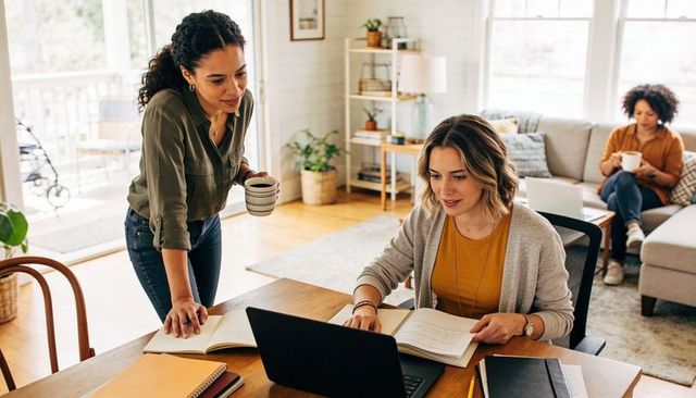 Women Collaborating Remotely in Bright Living Room Workspace, Laptop and Notebooks