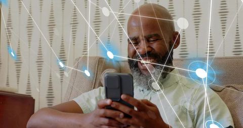 Smiling bearded bald senior man holding smartphone browsing with digital network overlay