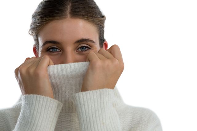 Portrait of woman covering face with turtleneck sweater against white background