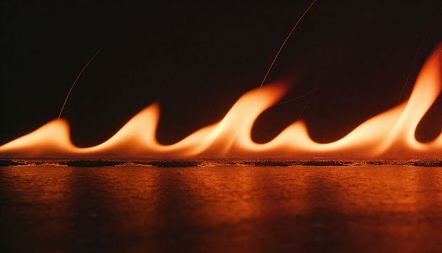 Burning low flame line lapping along asphalt with sparks and orange glowing reflection