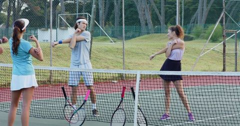 Warming up on tennis court: friends stretching pre-match with rackets and visors