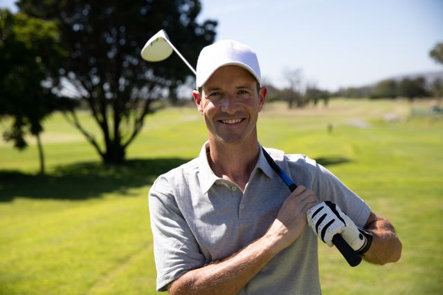 Portrait of Caucasian male golfer practicing on a golf course on a sunny day wearing a cap and golf clothes, holding a golf club on his shoulder. Hobby healthy lifestyle leisure.