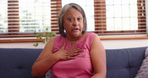 Senior woman in pink top expressing emotion on couch indoors