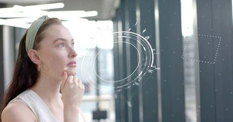 Contemplating businesswoman viewing futuristic holographic interface near glass corridor