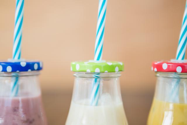 Close-up of three bottles filled with colorful smoothies, each topped with a polka dot lid and striped straw. Ideal for use in health and wellness blogs, summer refreshment promotions, or nutrition-related content.