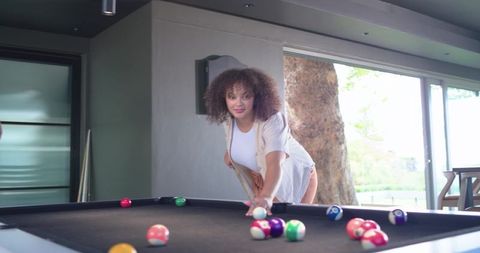 African american woman playing pool at home leaning over black felt table lining up shot