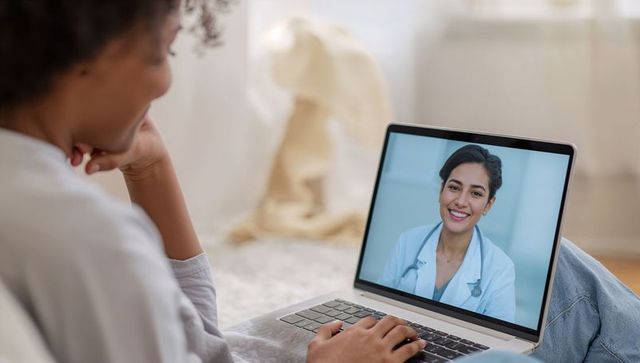 Young woman using laptop for telemedicine visit with smiling female physician at home